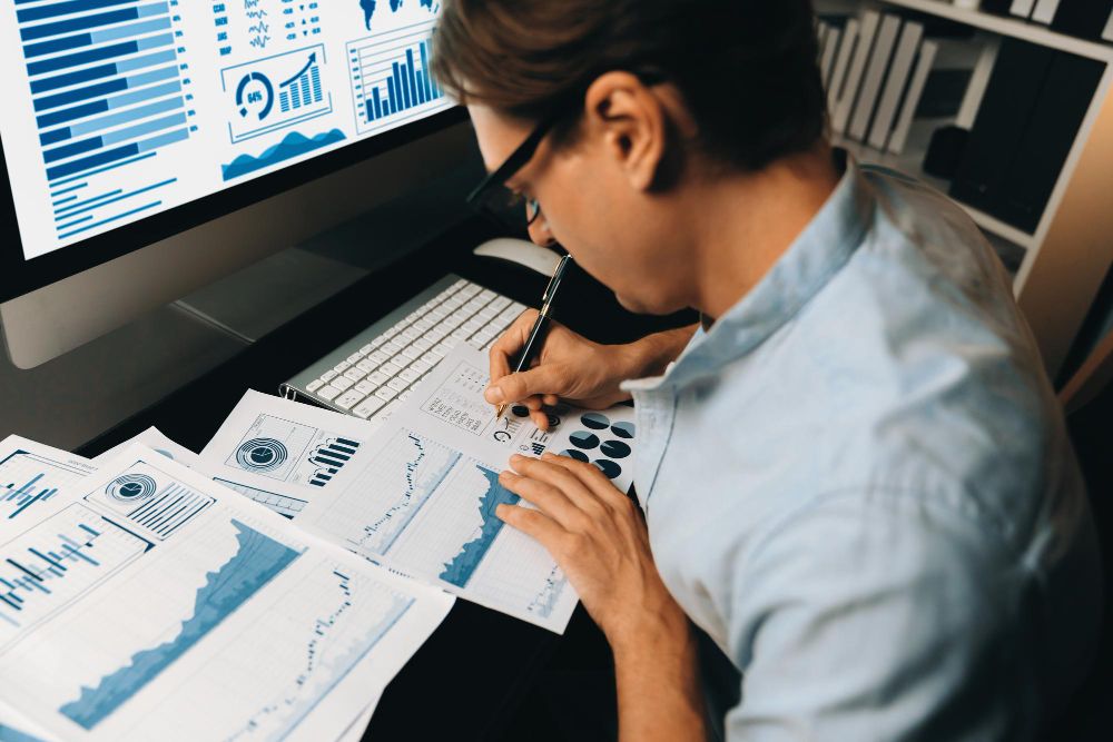 muskarac za radnim stolom analizira podatke poslovanja na papirima ispred njega